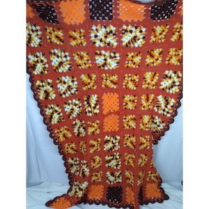 May include: A crocheted throw blanket with a brown, orange, and white geometric pattern. The blanket is made of squares and has a scalloped edge.