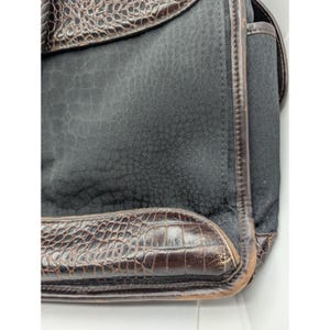 May include: A black leather bag with a crocodile embossed design. The bag has a flap closure and a brown leather trim.