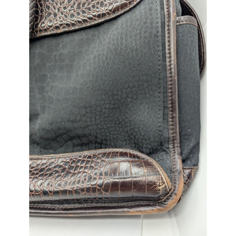 May include: A black leather bag with a crocodile embossed design. The bag has a flap closure and a brown leather trim.