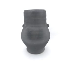 Può includere: Un piccolo vaso in ceramica nera con corpo arrotondato e un'ampia apertura. Il vaso ha due piccole maniglie sui lati.
