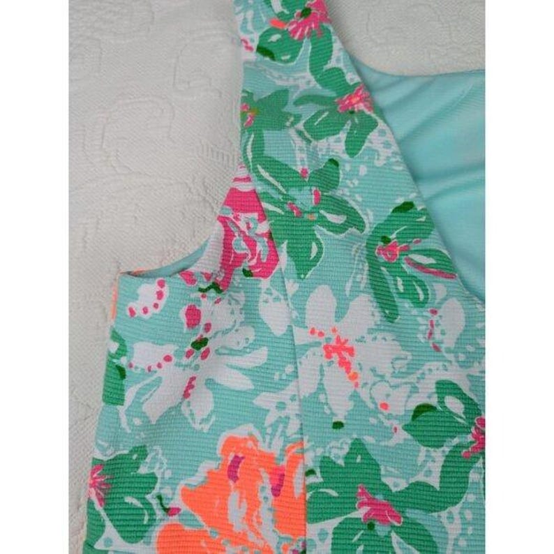 May include: A sleeveless dress with a floral pattern. The dress features a light blue background with large flowers in shades of green, white, pink, and orange. The fabric has a textured appearance.