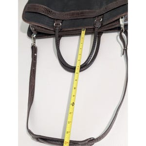May include: A brown leather briefcase with a long adjustable shoulder strap. The briefcase has two top handles and a zipper closure. The strap is measured with a tape measure, showing it is 16 inches long.