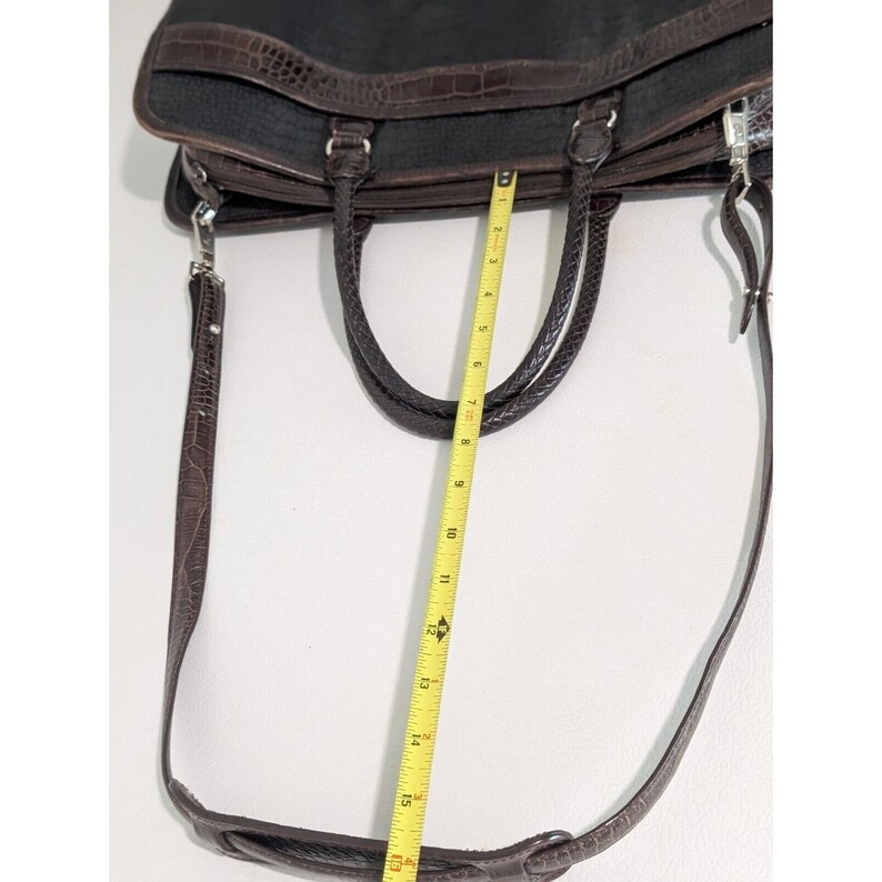 May include: A brown leather briefcase with a long adjustable shoulder strap. The briefcase has two top handles and a zipper closure. The strap is measured with a tape measure, showing it is 16 inches long.