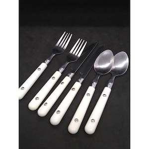 Könnte beinhalten: Sechsteiliges Besteckset mit weißen Griffen, bestehend aus zwei Gabeln, einem Messer und zwei Löffeln. Das Besteck ist aus Edelstahl und hat ein klassisches Design.