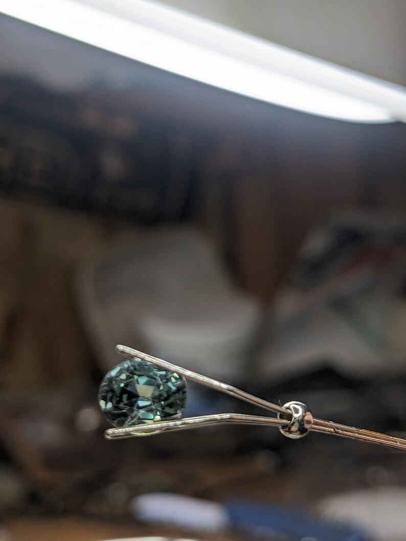 May include: A teal gemstone held in a pair of silver tweezers.