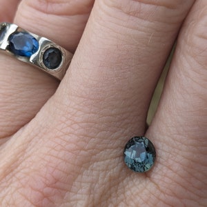 May include: A dark blue gemstone ring with a round cut. The ring is set in silver and has a textured band.
