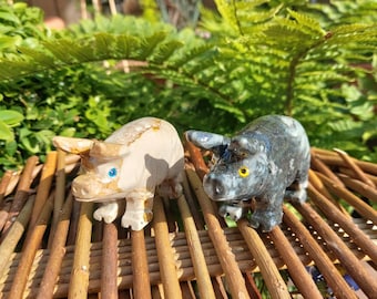 May include: Two small carved stone pig figurines. One is white with brown and black markings, the other is black with white markings. Both have blue eyes.