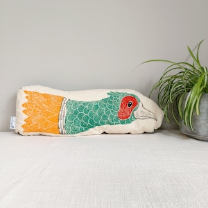 May include: A long, rectangular cushion with a printed design of a pheasant. The pheasant is green and yellow with a red head. The cushion is made of a soft, white fabric.