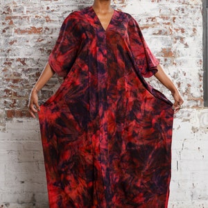 May include: A red and black tie-dye kaftan dress with a V-neckline. The dress has a flowing silhouette and is made of a soft, comfortable fabric.