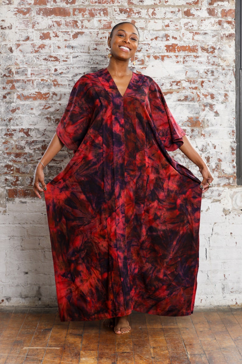 May include: A red and black tie-dye kaftan dress with a V-neckline. The dress has a flowing silhouette and is made of a soft, comfortable fabric.