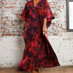 May include: A woman wearing a long, red and black tie-dye maxi dress with a V-neckline. The dress has a flowing silhouette and is made of a soft, comfortable fabric.