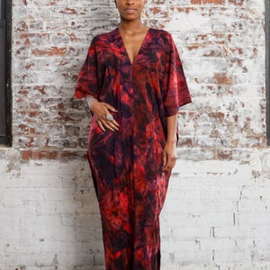 May include: A person wearing a red and black tie-dye kaftan with a deep V-neckline. The kaftan has a flowing silhouette and is made of a soft, comfortable fabric.
