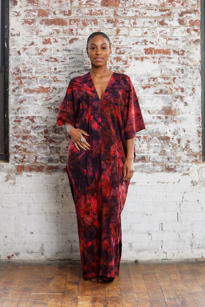 May include: A person wearing a red and black tie-dye kaftan with a deep V-neckline. The kaftan has a flowing silhouette and is made of a soft, comfortable fabric.