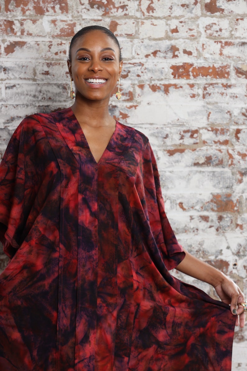 May include: A woman wearing a red and black tie-dye kaftan with a v-neck and short sleeves. The kaftan has a flowing silhouette and is made of a soft, silky fabric.