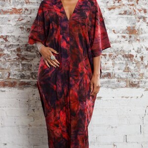 May include: A red and black tie-dye kaftan with a V-neckline. The kaftan is made of a soft, flowing fabric and has a relaxed fit.