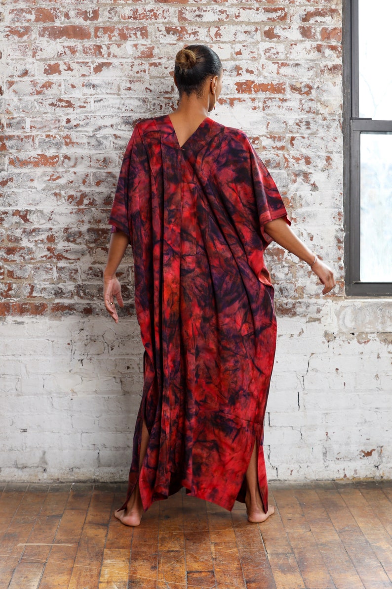 May include: A long, red and black tie-dye kaftan with side slits. The kaftan is made of a soft, flowing fabric.
