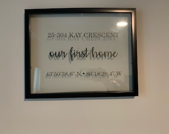 May include: A black framed picture with a white background and the text "25-304 KAY CRESCENT our first home 43°50′38.6" N 80°18′29.4" W" printed in black.