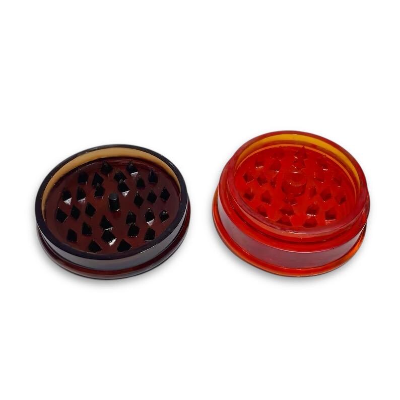 Puede incluir: Dos molinillos de hierbas de pl&aacute;stico, uno marr&oacute;n y otro rojo. Ambos molinillos tienen un patr&oacute;n de diamante en la parte inferior.