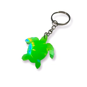 Può includere: Un portachiavi a forma di tartaruga marina verde con una finitura arcobaleno iridescente. Il portachiavi ha un anello e una catena in metallo argentato.