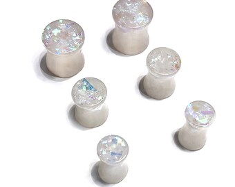 May include: Six white ear gauges with iridescent glitter embedded in the surface. The gauges are various sizes.