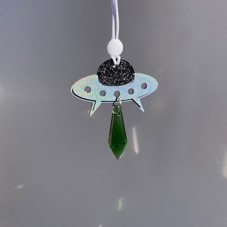 May include: A silver iridescent UFO charm with a black glitter top and a dangling green crystal pendant.