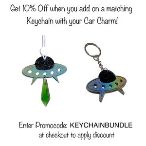 May include: Two iridescent blue and green UFO car charms. One charm is attached to a green crystal pendant and the other is attached to a silver key ring. The text "Enter Promocode: KEYCHAINBUNDLE at checkout to apply discount" is displayed below the charms.