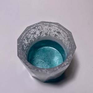 May include: A silver and teal geometric planter with a textured surface. The planter is empty and ready for a small plant.