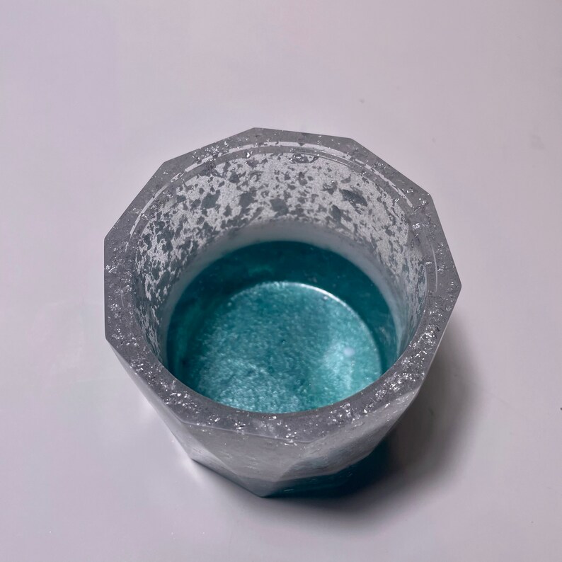 May include: A silver and teal geometric planter with a textured surface. The planter is empty and ready for a small plant.