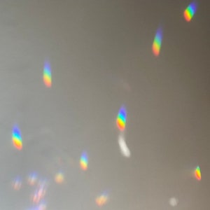 May include: A close-up of a light grey surface with multiple rainbow-coloured light reflections.