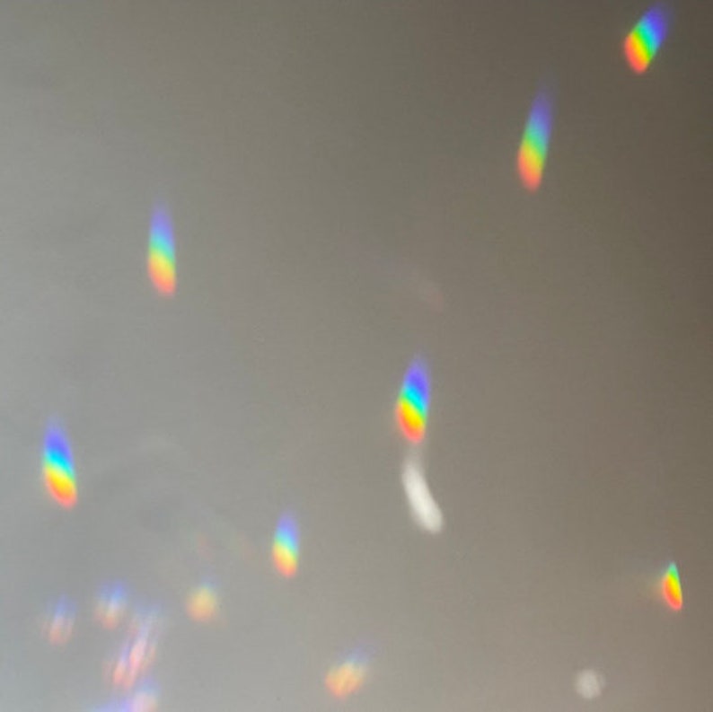 May include: A close-up of a light grey surface with multiple rainbow-coloured light reflections.
