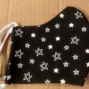 Pode incluir: Máscara facial preta com um padrão de estrelas brancas. A máscara tem laços elásticos para as orelhas.