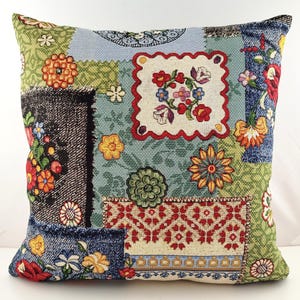 Pode incluir: Almofada decorativa quadrada com um design de patchwork. A almofada apresenta vários padrões florais em tons de azul, verde, vermelho, laranja e amarelo. A almofada tem uma aparência texturizada, com uma mistura de padrões florais e geométricos.