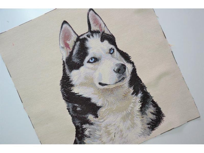 May include: A woven textile featuring a detailed portrait of a Siberian Husky dog. The dog has striking blue eyes, black and white fur, and a cream-colored background. The image is a close-up of the dog's head and shoulders.