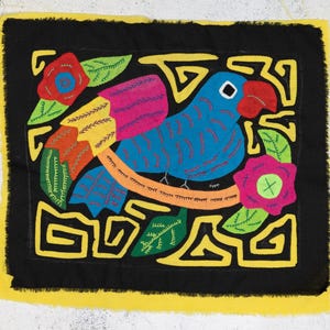 Peut inclure: Une tapisserie murale brodée colorée représentant un oiseau bleu avec un bec jaune et des accents rouges, entouré de fleurs et de feuilles. Le motif est sur un fond noir et encadré d'une bordure jaune.