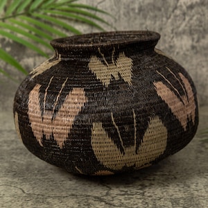 May include: A large, round, woven basket with a brown and beige pattern. The basket is made of natural materials and has a unique, hand-crafted look.