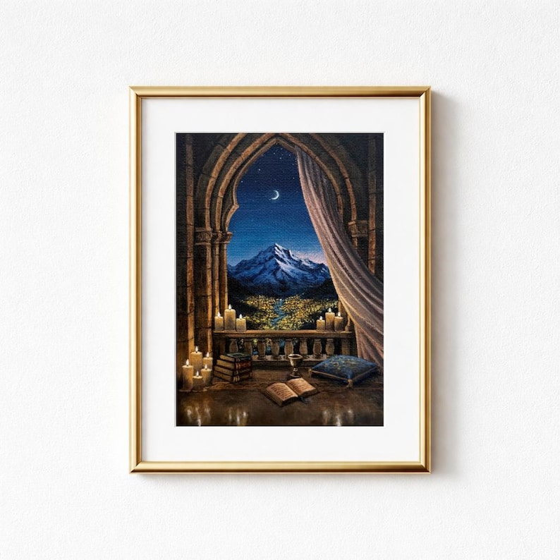 May include: A framed print depicts a nighttime mountain scene viewed through an arched window. The artwork features a crescent moon, candles, books, and a curtain. The color palette includes blues, golds, and browns, creating a cozy, inviting atmosphere.