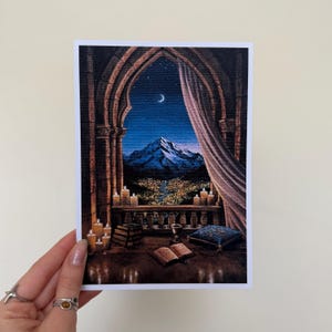 May include: A print of a nighttime mountain scene viewed through an arched window. The artwork features a starry sky, a crescent moon, and lit candles. A book and a decorative pillow are on the window ledge.