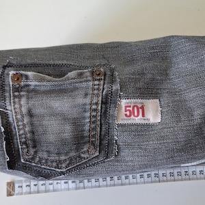 Könnte beinhalten: Grauer Jeansstoff mit einer Tasche und einem Levi's Original 501 Straight Fit-Etikett. Der Stoff ist gefaltet und mit einem Maßband gemessen.
