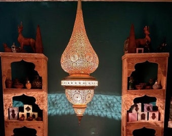 May include: An ornate, teardrop-shaped pendant lamp with a warm, golden glow hangs in the center of the image. Two wooden shelves flank the lamp, each displaying decorative items and colorful cubes. The scene is set on a patterned rug.