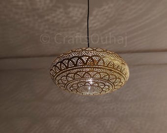 Może przedstawiać: Mosiężna lampa wisząca z misternym, ażurowym wzorem. Owalna lampa zawieszona jest na czarnym kablu. Wewnętrzne światło rzuca dekoracyjne cienie. Ozdobny przedmiot do oświetlenia wnętrz.