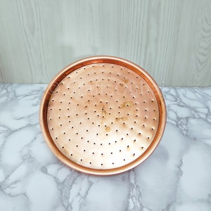 May include: A round copper tray with a perforated surface. The tray has a smooth, shiny finish and is ideal for serving or displaying items.