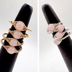 May include: Two sets of stacked rings with pink stones wrapped in wire. One set is gold and the other is silver.