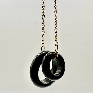 May include: A gold chain necklace with two black, interlocking rings as a pendant.