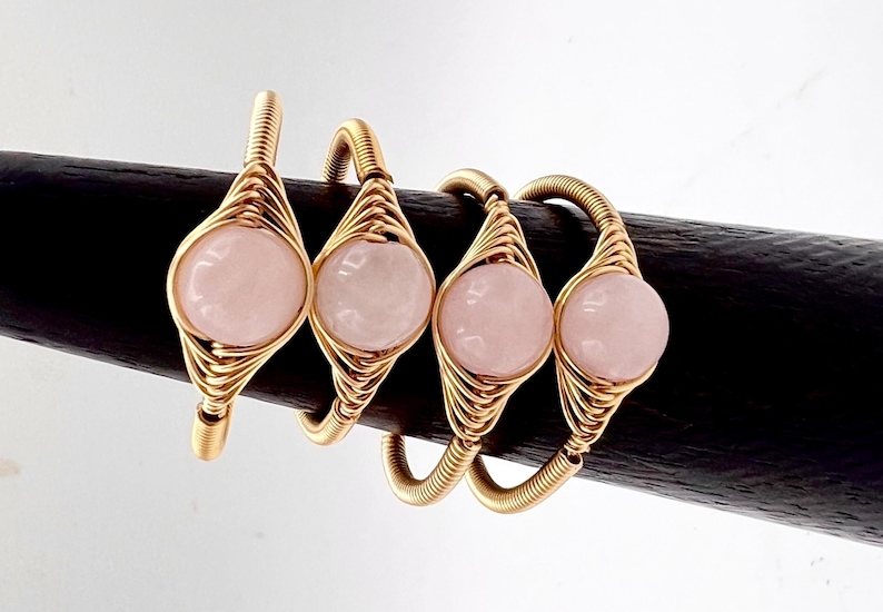 May include: Four gold wire wrapped rings with pink rose quartz stones. Each ring features a delicate wire design and a smooth, round stone.