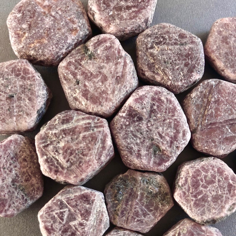 K&ouml;nnte beinhalten: Eine Sammlung von 12 facettierten Rubin-Steinen, jeder mit einer einzigartigen Form und Gr&ouml;&szlig;e. Die Steine sind tiefrot mit einem leichten violetten Farbton. Sie sind alle poliert und haben eine glatte, gl&auml;nzende Oberfl&auml;che.