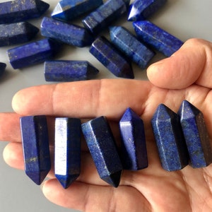 May include: A collection of small, dark blue lapis lazuli crystal points. The points are smooth and polished, with a slight sparkle. The points are arranged in a hand, with the tips pointing upwards.