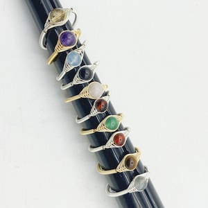 May include: A set of ten wire-wrapped rings with different colored gemstones. The rings are stacked on a black surface. The gemstones include clear, amethyst, blue, black, pink, green, red, brown, gold, and gray.