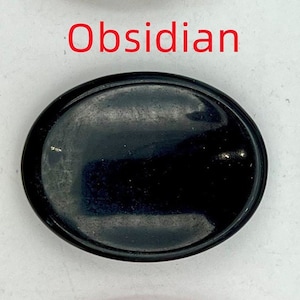 K&ouml;nnte beinhalten: Ovaler Obsidian-Stein mit glatter, polierter Oberfl&auml;che. Der Stein ist schwarz und hat einen leichten Glanz.