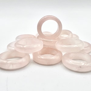 May include: A pile of pink rose quartz rings. The rings are smooth and polished, and they are all the same size.