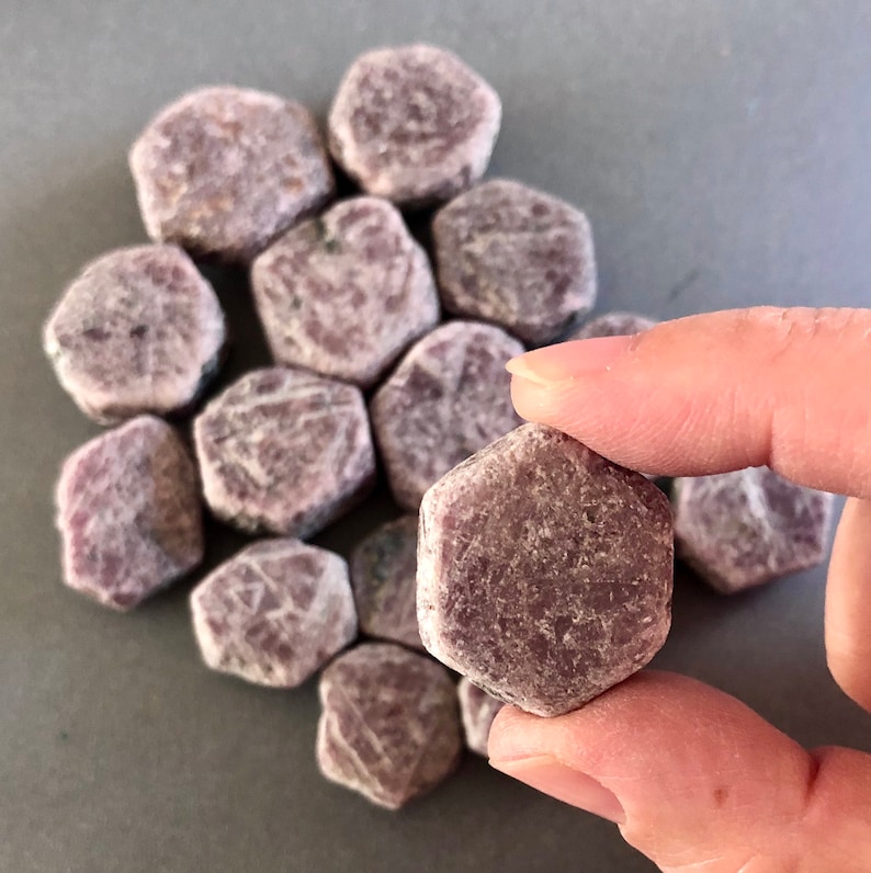 K&ouml;nnte beinhalten: Eine Sammlung kleiner, facettierter, rosafarbener Rubinkristalle. Die Kristalle sind sechseckig und haben eine raue, nat&uuml;rliche Textur.